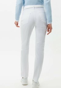 Jeans blancos ajustados con una textura suave, con una cintura de altura media, dos bolsillos traseros y detalles de costura sutiles. Combinados con zapatillas blancas.