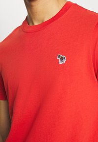 Camiseta de algodón roja con cuello redondo. Presenta un pequeño logo de caballo multicolor bordado en el lado izquierdo del pecho.