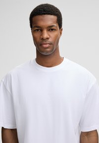 Weißes Baumwoll-T-Shirt mit lockerem Schnitt. Verfügt über einen Rundhalsausschnitt und kurze Ärmel. Glatte Textur, ohne sichtbare Muster oder Akzente.