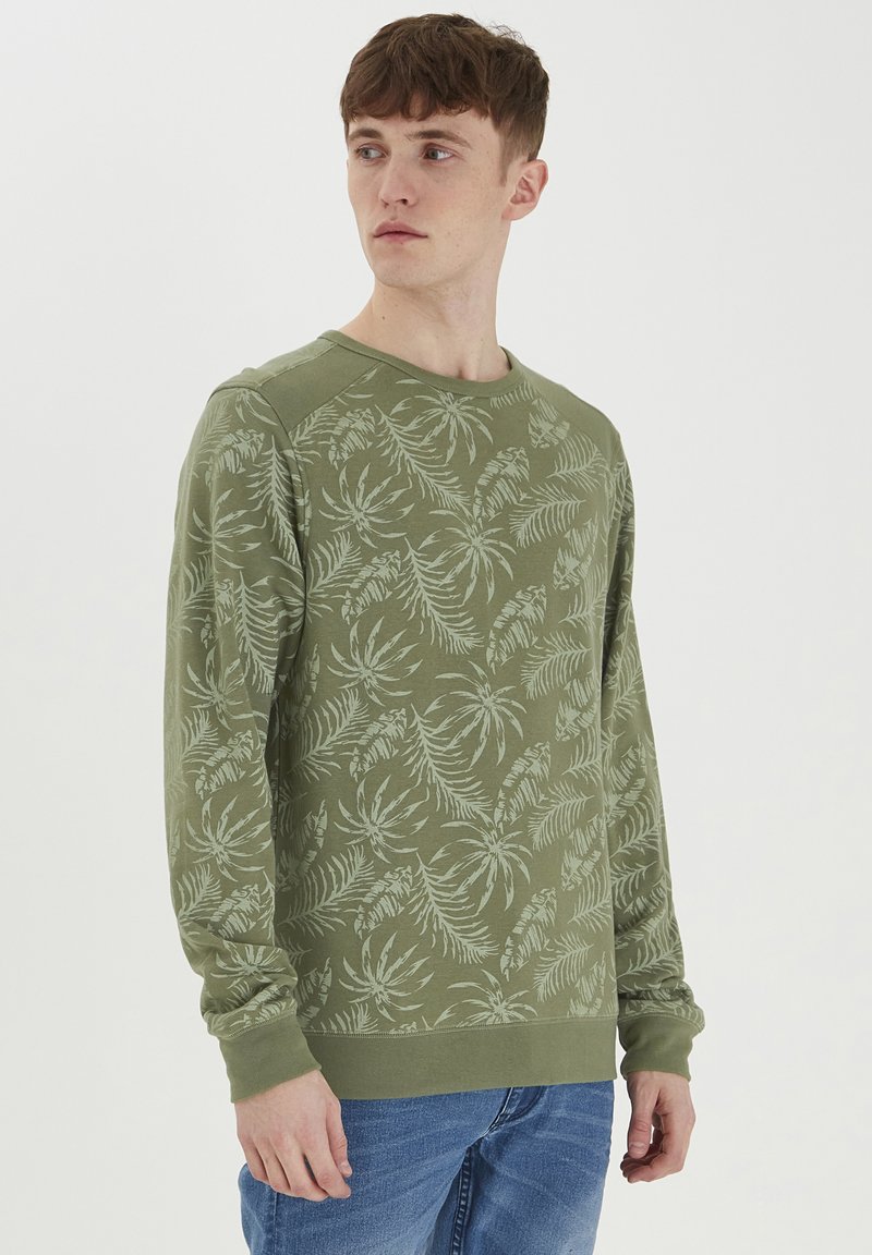 Sudadera verde con un patrón de hojas, cuello redondo y puños de canalé. Fabricada en material suave, presenta un ajuste holgado y mangas raglán.