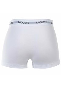 Białe bawełniane bokserki z szaro-skalanym pasem, na którym znajduje się napis "LACOSTE" w czarnym kolorze. Gładka tekstura, dopasowany krój, długość do połowy uda.