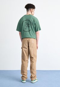 Groene t-shirt met zwarte print met een cartoonontwerp; beige cargobroek met zakken; sneakers met groene accenten.