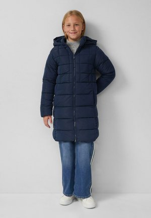 Marineblauer Puffer-Mantel mit Kapuze, ausgestattet mit einem gesteppten Design, Frontreißverschluss und langen Ärmeln, getragen über blauen Jeans und weißen Sneakern.
