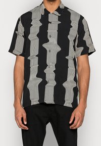 Camicia nera a maniche corte con motivo di linee bianche ondulate. Materiale leggero. Colletto classico con chiusura frontale con bottoni.