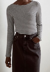 Schwarz-weiß gestreiftes Langarmoberteil, kombiniert mit einem hoch taillierten dunkelblauen Denimrock mit vorderen Taschen und einem Knopfverschluss.