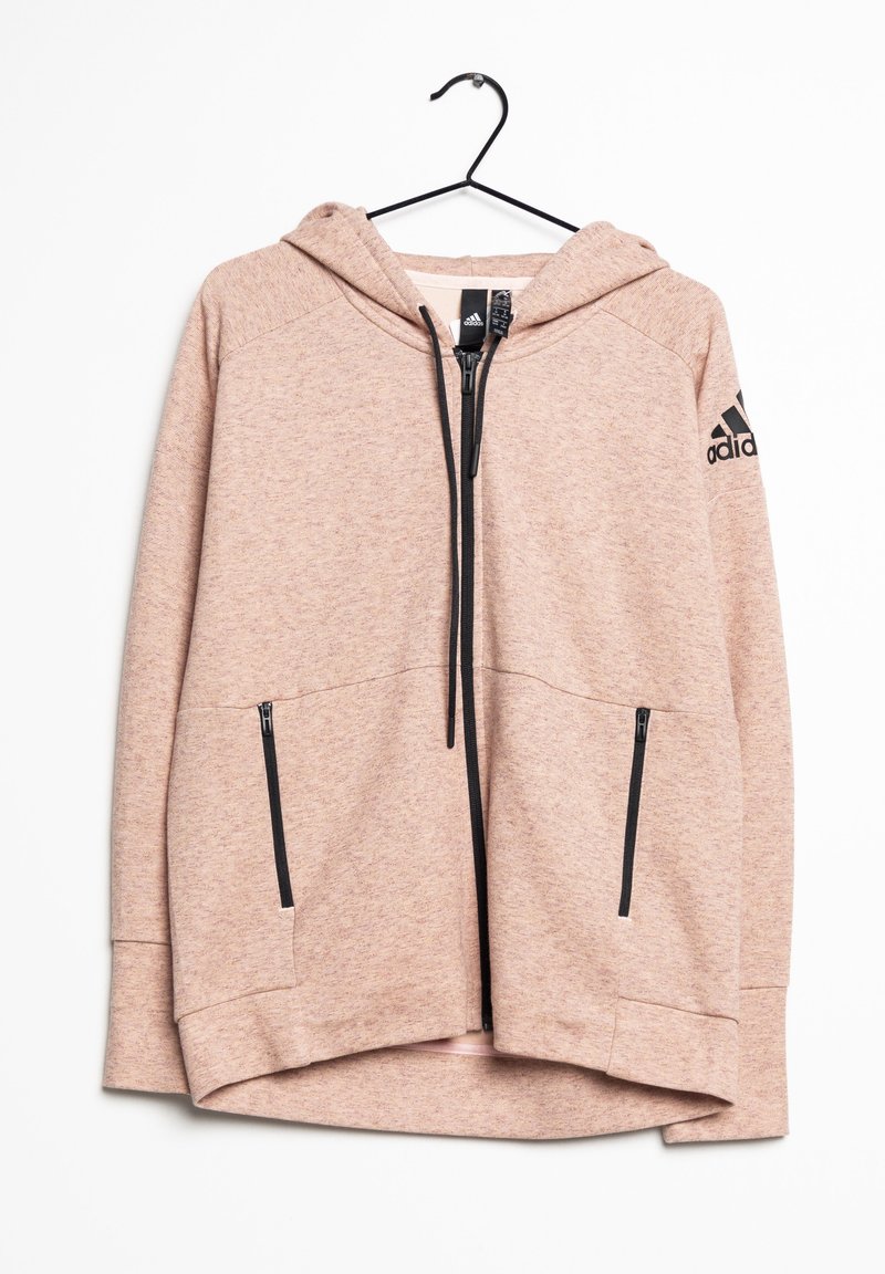 Sweatshirt à capuche rose clair en tissu texturé, avec une fermeture éclair à l'avant, deux poches zippées noires et un logo noir sur la manche gauche.