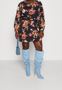 Květinové šaty s dlouhým rukávem na námořnickém pozadí, s vypasovaným pasem, spárované s volnými světle modrými kottmi do kolen a odpovídající mini taškou.