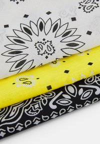 Trois tissus empilés : le dessus est blanc avec des motifs floraux noirs, le milieu est jaune vif avec des éléments de design noirs, et le bas est noir avec des motifs paisley blancs.