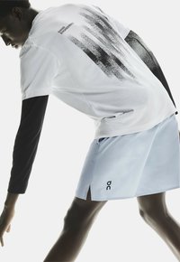 Witte shirt met een zwart printontwerp, lange zwarte mouwen en lichtblauwe shorts met zijsluitingen en branding op de zoom.