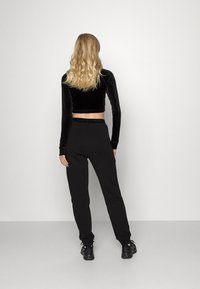 Černý sametový crop top a černé tepláky z pohledu zezadu, s přiléhavým stylem a stahovacími šňůrkami v pase, doplněné o černé tenisky.