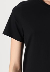 Sort bomulds-T-shirt med rund hals, korte ærmer og glat tekstur. Har sømløse skuldre og en klassisk pasform.