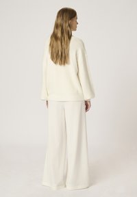 Pull en maille côtelée de couleur crème associé à un pantalon large off-white. Texture douce et coupe décontractée dans l'ensemble de l'accoutrement.