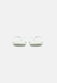 Vita flip-flops med tunna remmar och en strukturerad sula. Har en flerfärgad randig design på sulan.