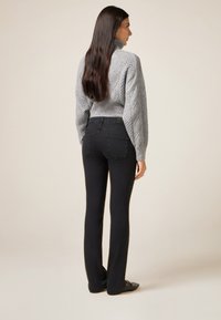 Jersey gris de punto con cuello alto y patrón de diamantes, combinado con vaqueros negros acampanados con costuras decorativas en los laterales.