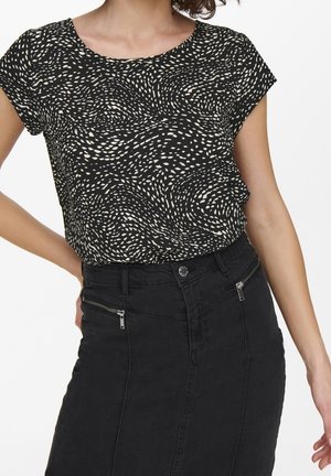 Woman wearing a black and white patterned short-sleeve top tucked into a high-waisted black skirt with front zip pockets.