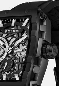 Zwart metalen horloge met een skelet-dial. Heeft zilveren accenten, chronograaf sub-dials en een getextureerde rubberen band. Toont de dagen van de week.