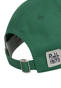 Gorra de béisbol de algodón verde con una etiqueta cosida que dice "PJL Club 1973". Tiene un visera curvada y un ajuste de hebilla metálica en la parte de atrás.