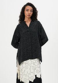 Schwarzes Hemd mit Blumenmuster, mit Kragen und langen Ärmeln. Das Material wirkt leicht und hat eine glatte Textur.
