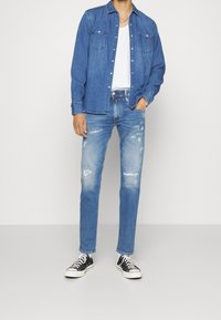 Denim shirt with button front, two chest pockets, and long sleeves; paired with light blue distressed jeans and black sneakers.