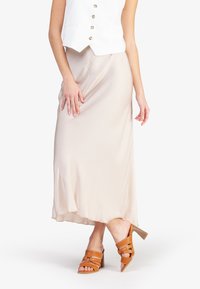 Beige satin maxiskørt med let svajet kant, parret med brune strop-sandaler med hæl, som har en firkantet hæl og åben tå-design.