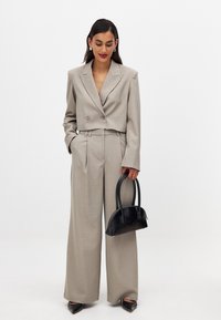 Beige cropped blazer with double buttons and wide-leg trousers; paired with a small black textured handbag and pointed black heels.