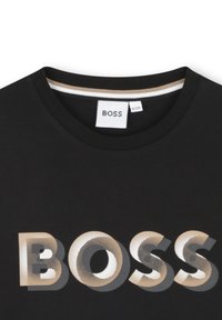 Zwarte t-shirt met een ronde halslijn en korte mouwen. De voorkant toont een groot "BOSS" logo in goud met een stippenpatroon.