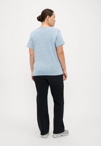 Camisola de malha de manga curta azul clara com um corte descontraído, combinada com calças pretas. A camisola possui um decote redondo e uma textura subtil.