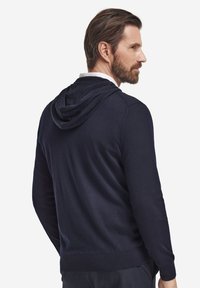 Mörkblå hoodie i mjukt material, med avslappnad passform, en känguruficka samt ribbade muddar och fåll. Huvan är fastsydd bak.