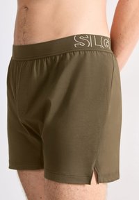Olijf groene boxershorts met een gladde textuur, elastische tailleband met het "SILG" logo en zijsplitsingen voor extra comfort.