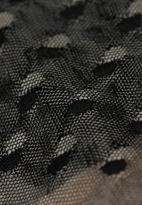 Zwarte kantstof met een hexagonaal gaaspatroon en gematerialiseerde cirkels van verschillende groottes, wat een gelaagd en ingewikkeld ontwerp creëert.