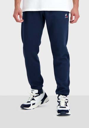 Pantaloni tuta navy realizzati in morbido tessuto, con una vita elastica e tasche laterali. Un logo è ricamato sulla coscia sinistra.