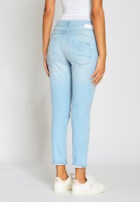 Světle modré džíny s úzkým střihem, které mají zadní kapsy a detaily v prošívání. Nosit se s bílými teniskami.