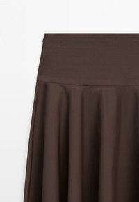 Mørkebrun nederdel med bred, syet taljebånd og bløde plisseringer nedenunder, hængende mod en ensartet hvid baggrund.