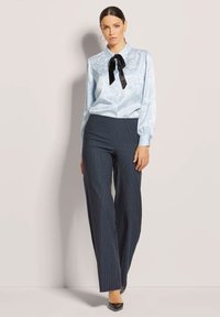 Lichtblauwe blouse met bloemenpatroon en zwarte strik, gecombineerd met donker gestreepte wijde broek en zwarte puntige hakken.