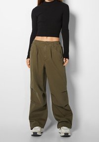 Maglietta cropped nera a coste con maniche lunghe abbinata a pantaloni cargo larghi di colore verde oliva con vita elastica e tasche laterali.