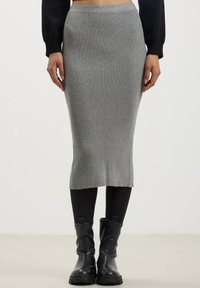 Gonna midi grigia a coste con una silhouette aderente, caratterizzata da una vita liscia e uno spacco laterale, abbinata a stivali alla caviglia in pelle nera.