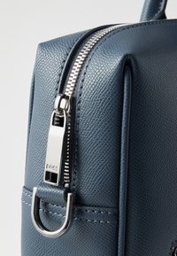 Μπλε υφασμάτινη δερμάτινη τσάντα με ασημένιο φερμουάρ και μεταλλικά στοιχεία. Διαθέτει πλευρικό βρόχο για εύκολη μεταφορά. Συμπαγής, δομημένος σχεδιασμός.