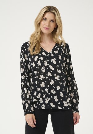 Blouse noire avec motif floral blanc, col en V, manches longues et tissu doux avec texture. Coupe décontractée, adaptée à diverses occasions.