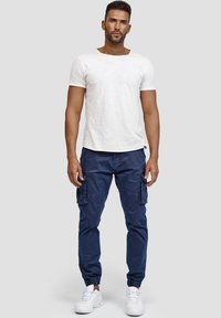 Camiseta blanca de manga corta con escote redondo, combinada con joggers cargo azul oscuro con puños elásticos y bolsillos laterales; zapatillas blancas.