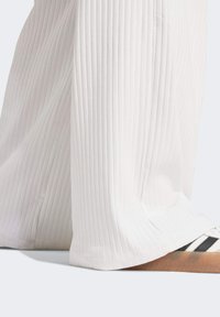 Vita, ribbade byxor med vida ben, texturerad yta och avslappnad passform. Matchas med vita sneakers med svarta ränder.