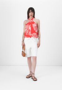 Red halter top with white abstract pattern, paired with white shorts and brown strappy sandals. Brown handbag as an accessory.