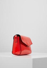 Bolso de piel sintética roja con forma estructurada, solapa plegable y ribete negro en contraste. Textura suave, tamaño compacto adecuado para lo esencial.