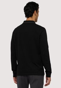 Czarna koszulka polo z długim rękawem i kołnierzykiem, z przeszyciem na tylnej części i rozcięciami po bokach. Wykonana z miękkiego materiału o gładkiej fakturze.