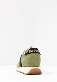 Vihreät samettiset lenkkarit mustilla yksityiskohdilla, kangaspäällysteellä ja valkoisella välipohjalla. Kengissä on kultainen "SAUCONY" -teksti mustassa kantapääosassa.