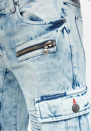 Lichtblauwe denim cargobroek met een vervaagde, versleten uitstraling. Voorzien van een ritszak en een logo-opname met rode stikaccenten.