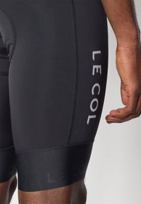 Schwarze Radshorts aus dehnbarem Material mit grauem Branding "LE COL", flachen Nähten und einer enganliegenden Passform.