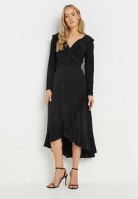 Czarna sukienka o kroju kopertowym z długimi rękawami, falbaniastym kołnierzykiem i asymetrycznym dołem. Wykonana z miękkiego materiału, z warstwowym detalem falbanek.