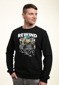 Sweatshirt nero con una stampa grafica di un personaggio con accenti turchesi e arancioni, testo bianco in grassetto e firma in stile graffiti.