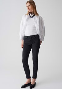 Un jean skinny noir associé à une chemise blanche à boutons et à une écharpe en couches noire et brune. Textures lisses et design ajusté.