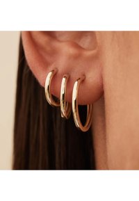 Boucles d'oreilles créoles dorées avec trois tailles graduées. Surface lisse et brillante avec une finition polie. Portées sur le lobe, elles épousent l'oreille de manière sécurisée.